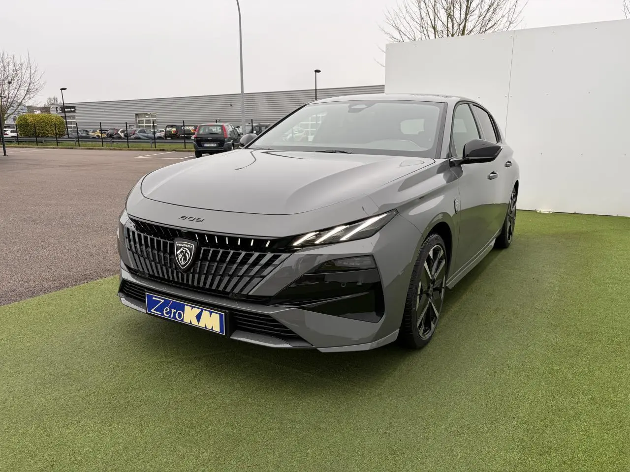 Peugeot 308 gris selenium vue 3/4 avant droit, calandre noire avec logo lion et jantes alliage noires.