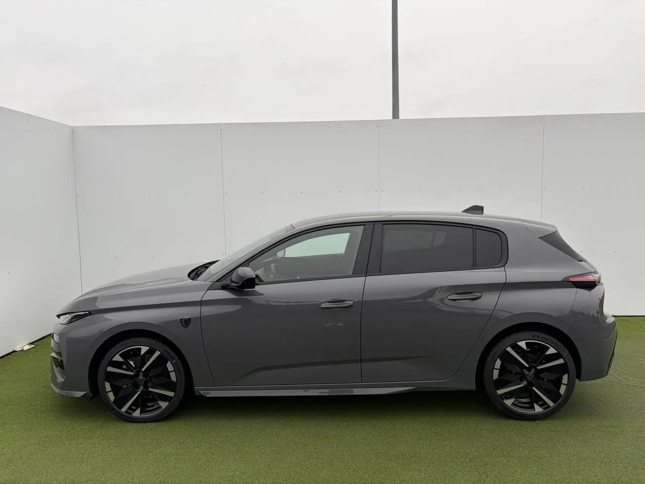 Profil droit d'une Peugeot 308 III hybride 2025 gris selenium avec jantes alliage noires et vitres surteintées.
