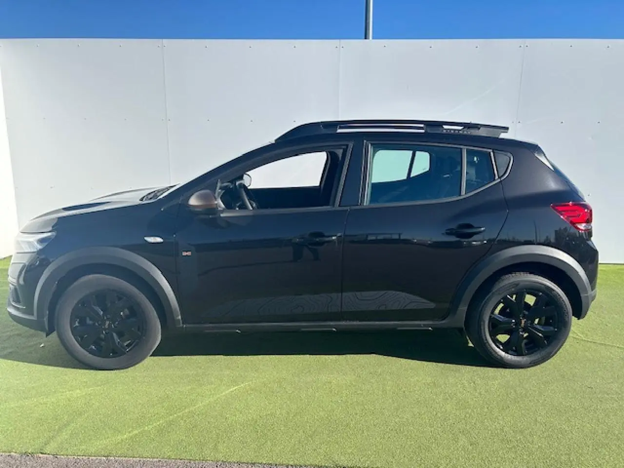 Vue de profil côté gauche d'une Dacia Sandero III Stepway noire nacrée avec jantes noires et barres de toit.