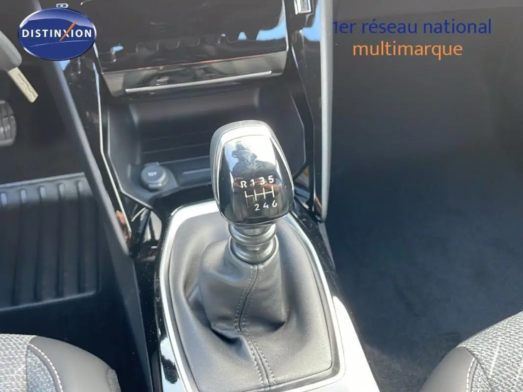 Gros plan sur le levier de vitesse manuel noir du Peugeot 2008 gris, avec console centrale brillante en arrière-plan.