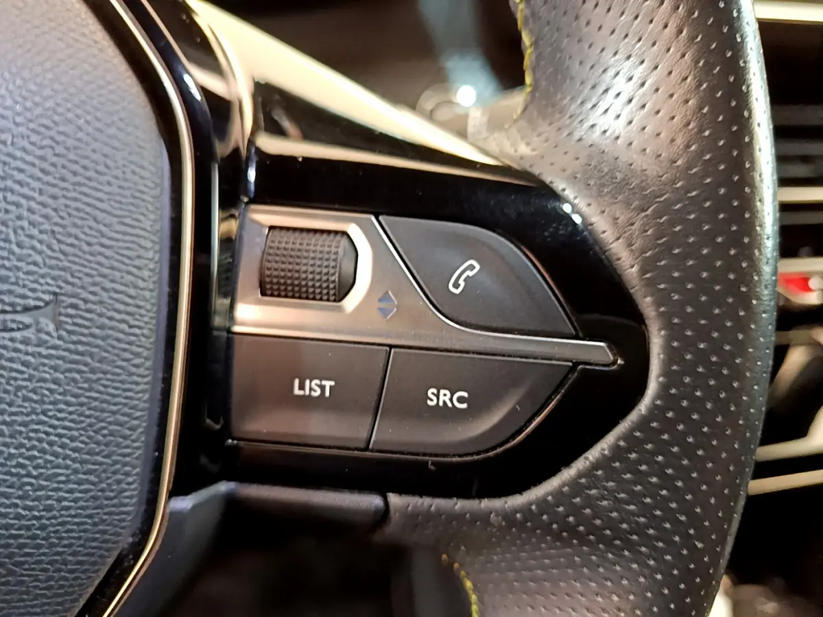 Gros plan sur les commandes gauche du volant en cuir perforé du Peugeot 208 GT Line rouge, boutons téléphonie et navigation.