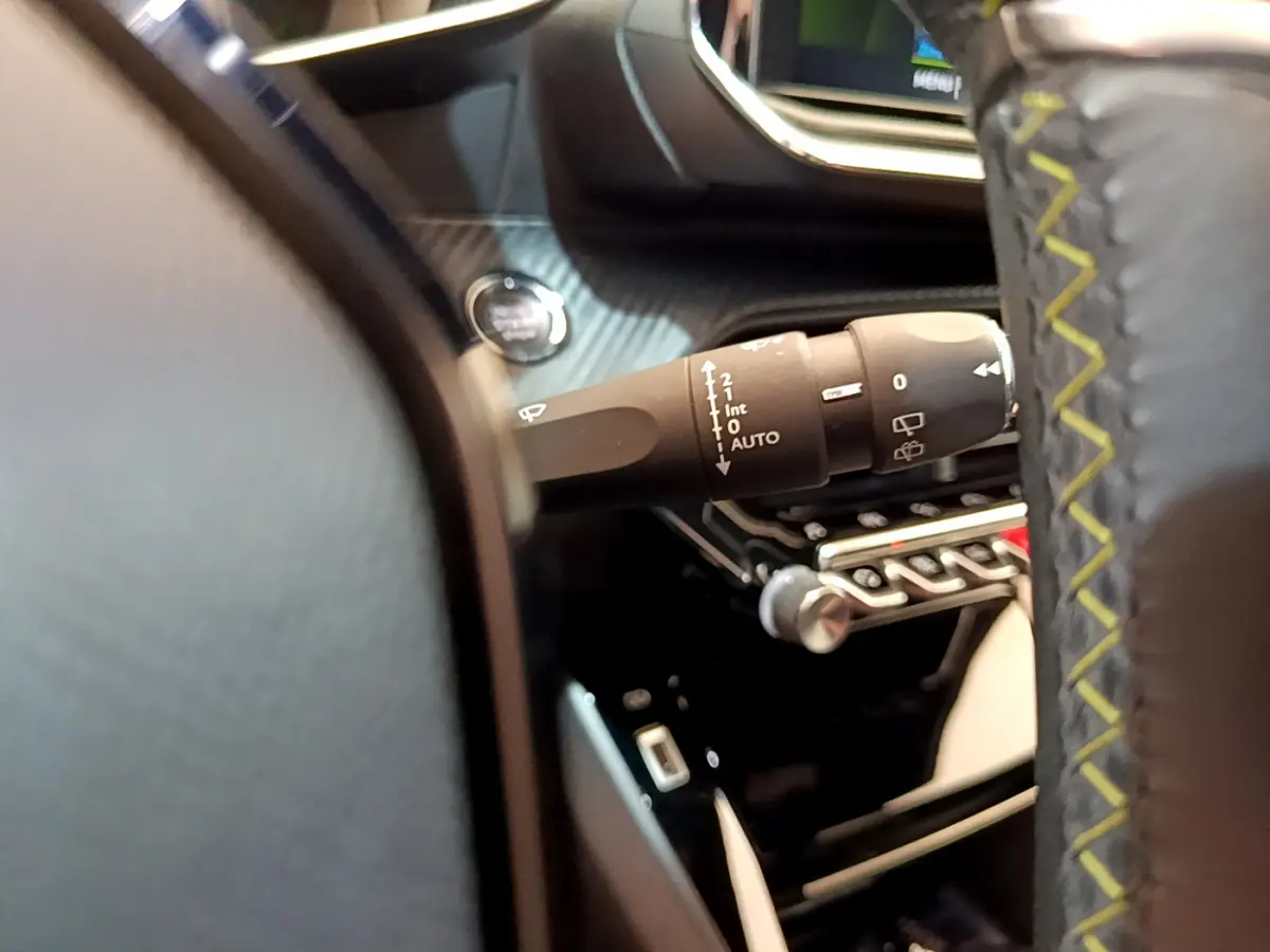 Gros plan sur la manette d’essuie-glace à gauche du volant cuir noir avec surpiqûres jaunes dans une Peugeot 208 rouge.