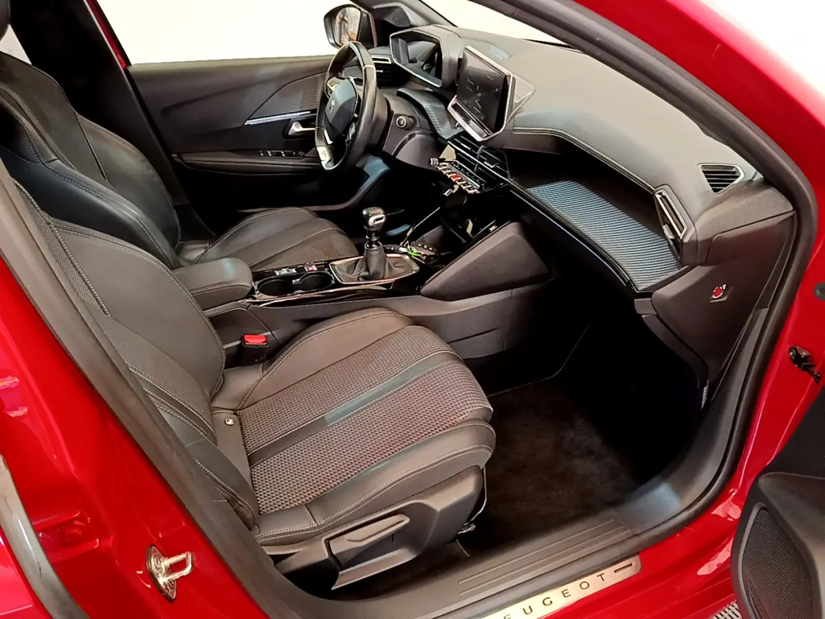 Intérieur côté conducteur d'une Peugeot 208 rouge, montrant sièges en cuir, volant multifonctions et tableau de bord moderne.