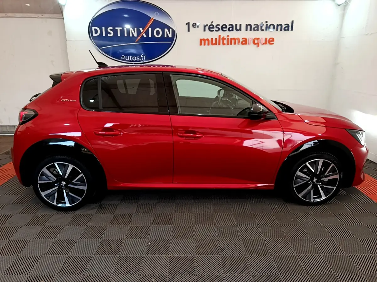 Profil côté gauche d'une Peugeot 208 GT Line rouge 2020 avec jantes alliage et vitres teintées en intérieur showroom.