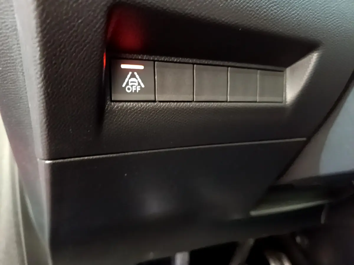 Gros plan sur le bouton de désactivation de l'assistance au maintien de voie dans l'habitacle noir d'une Peugeot 208 rouge