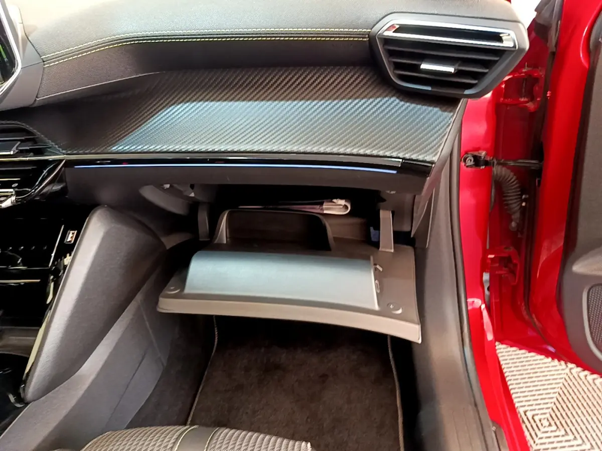 Vue intérieure côté passager du Peugeot 208 GT Line rouge 2020 avec boîte à gants ouverte et tableau de bord noir.
