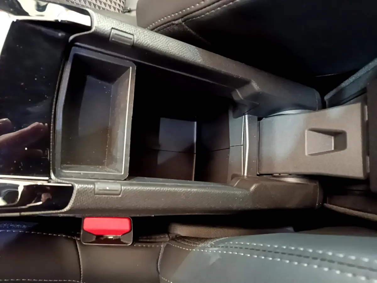 Vue plongeante sur le rangement central noir ouvert de la Peugeot 208 GT Line rouge, avec bouton de frein à main visible.