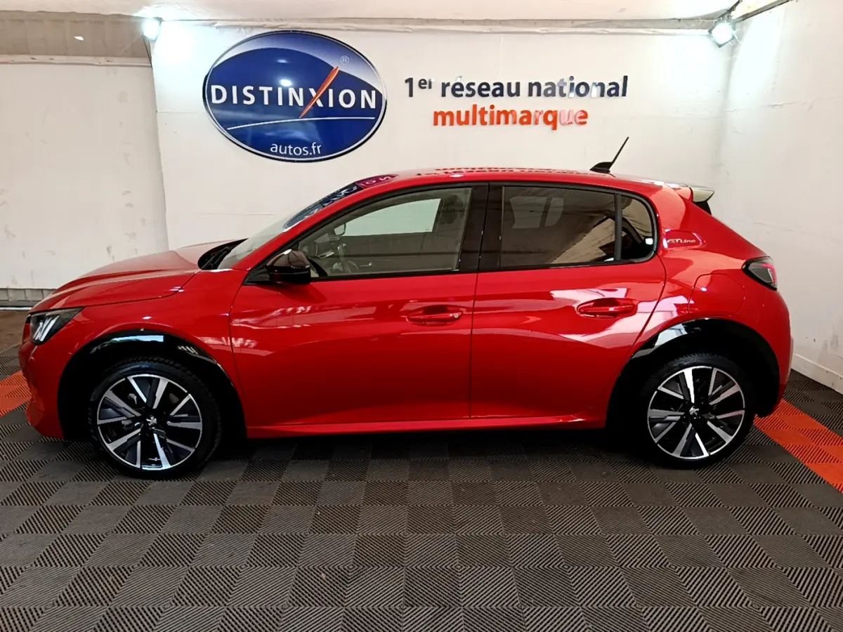 Profil côté gauche d'une Peugeot 208 GT Line rouge de 2020, avec jantes alliage et vitres teintées en intérieur showroom.
