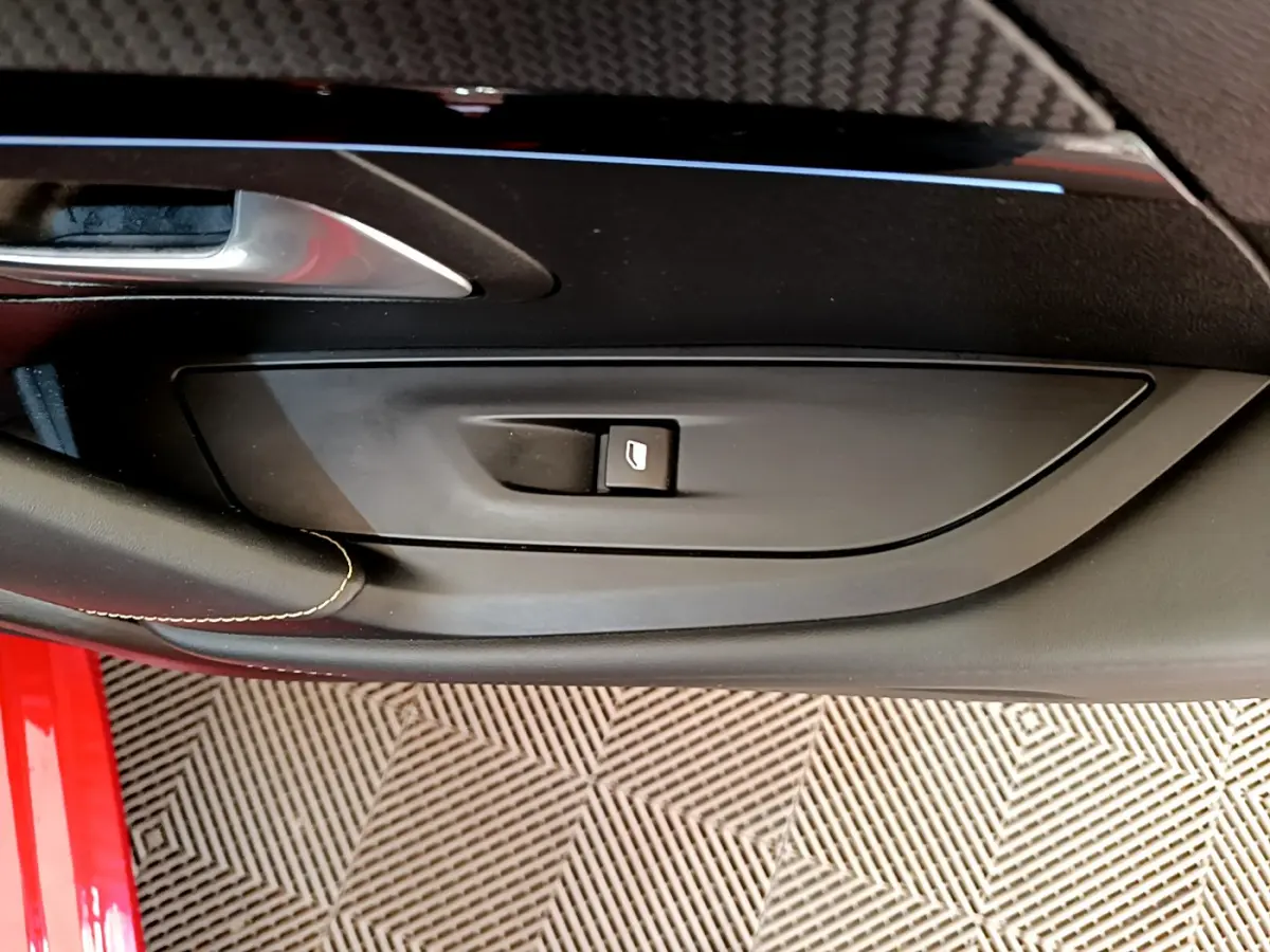 Gros plan sur la commande de lève-vitre côté gauche de la porte intérieure d’une Peugeot 208 rouge.