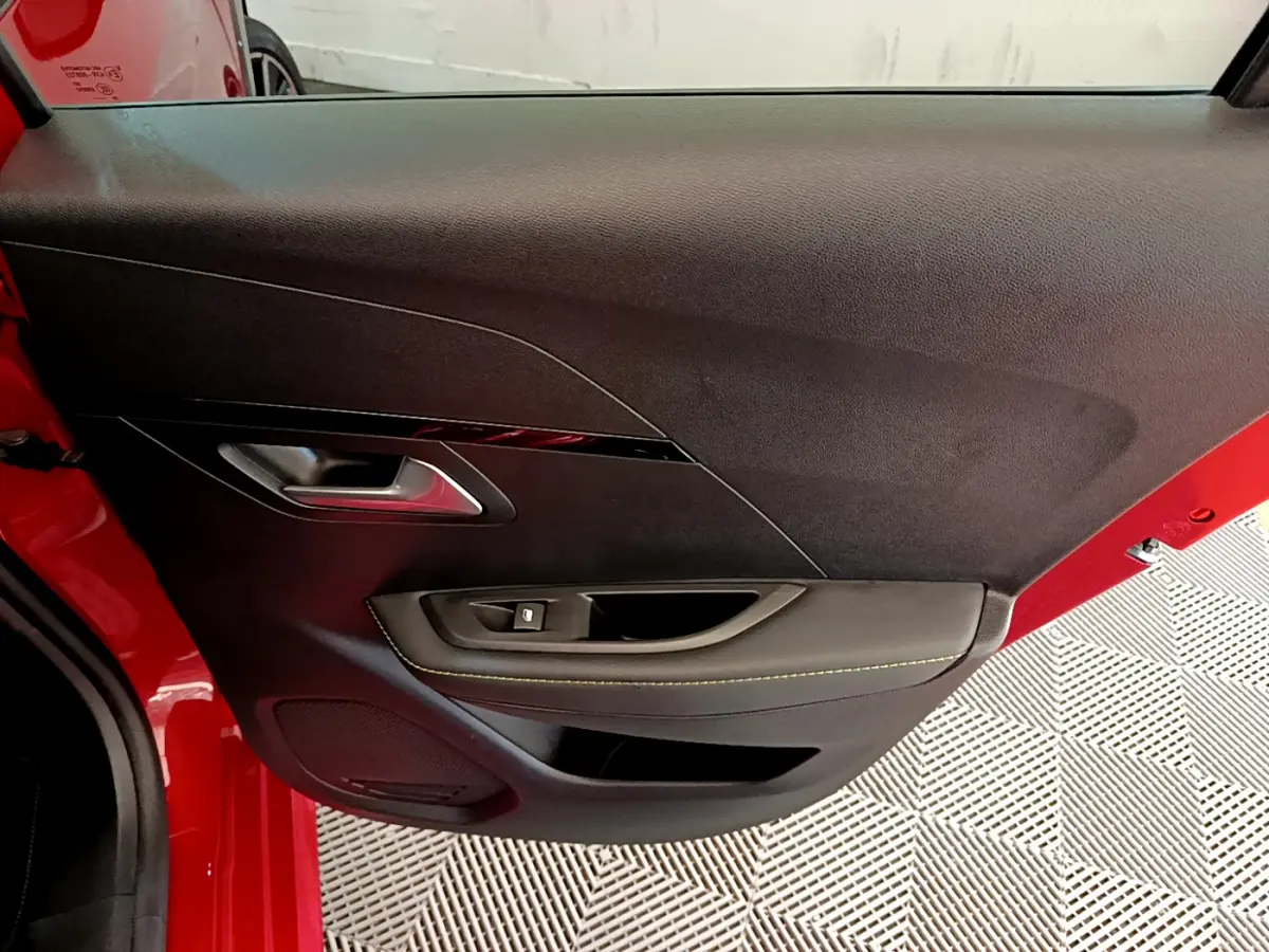 Vue rapprochée de la porte avant gauche rouge d'une Peugeot 208 GT Line avec garniture noire et surpiqûres jaunes.