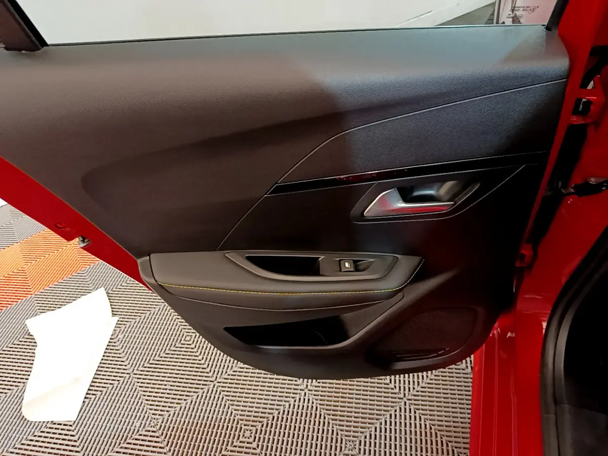 Vue intérieure de la porte arrière gauche rouge de la Peugeot 208 GT Line avec poignée argentée et bouton de vitre électrique.