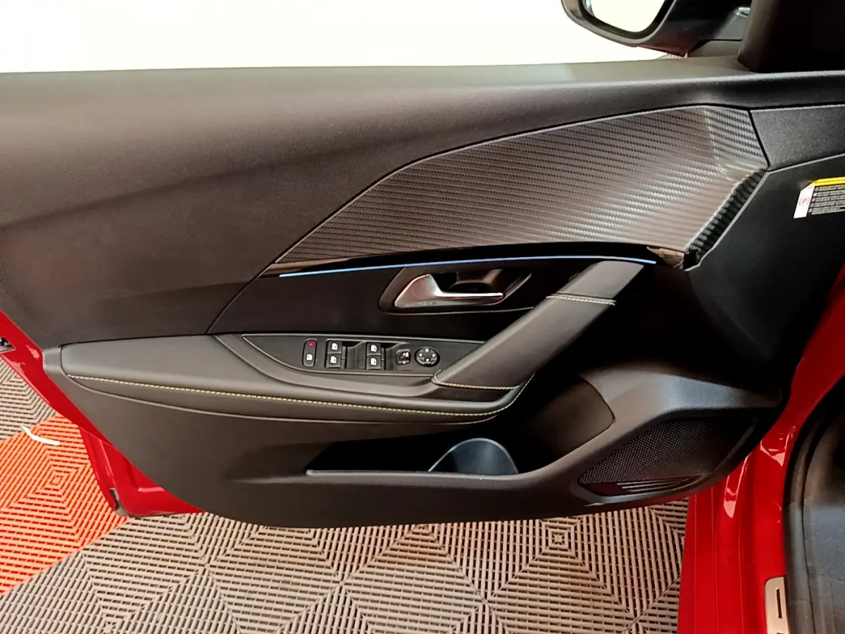 Vue rapprochée de la porte avant gauche rouge d'une Peugeot 208 GT Line avec garniture noire et surpiqûres contrastées.