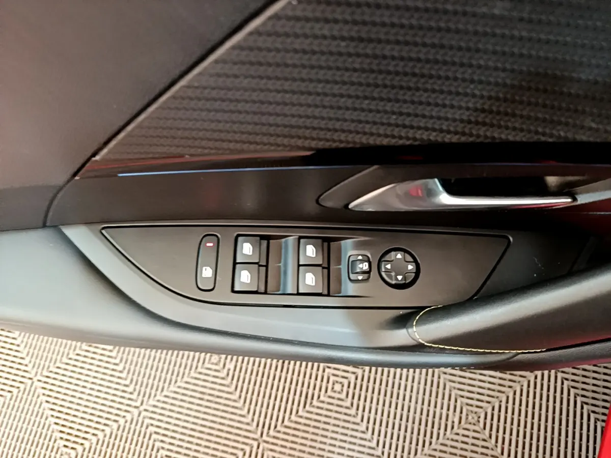 Gros plan sur la commande des vitres et rétroviseurs côté conducteur d'une Peugeot 208 rouge, finition GT Line.