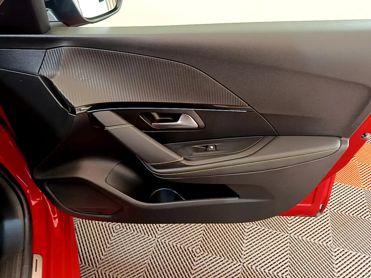 Vue rapprochée de la porte avant gauche rouge d'une Peugeot 208 GT Line avec garniture noire et surpiqûres jaunes.