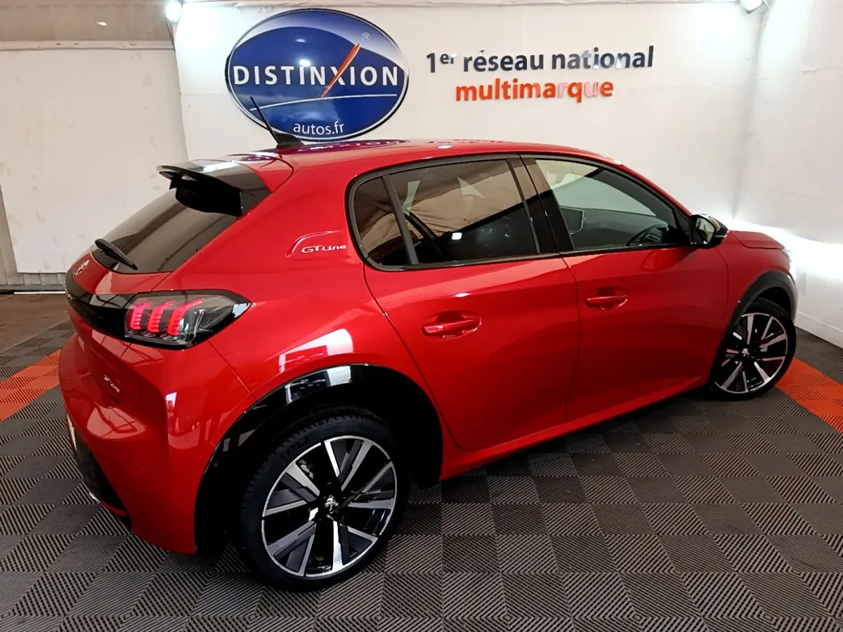Vue 3/4 arrière droite d'une Peugeot 208 GT Line rouge avec jantes alliage et vitres teintées dans un showroom