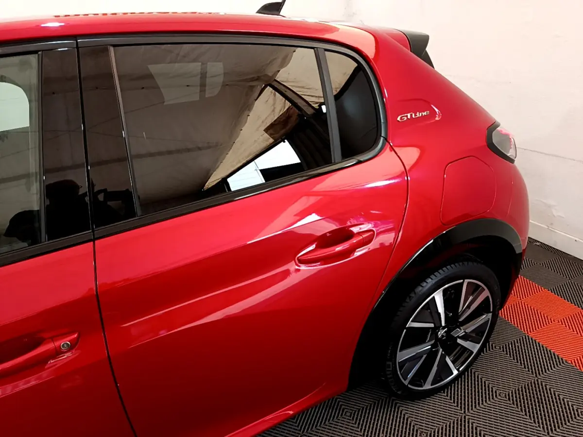 Vue côté droit arrière d'une Peugeot 208 GT Line rouge avec jante alliage et logo GT Line sur l'aile arrière.