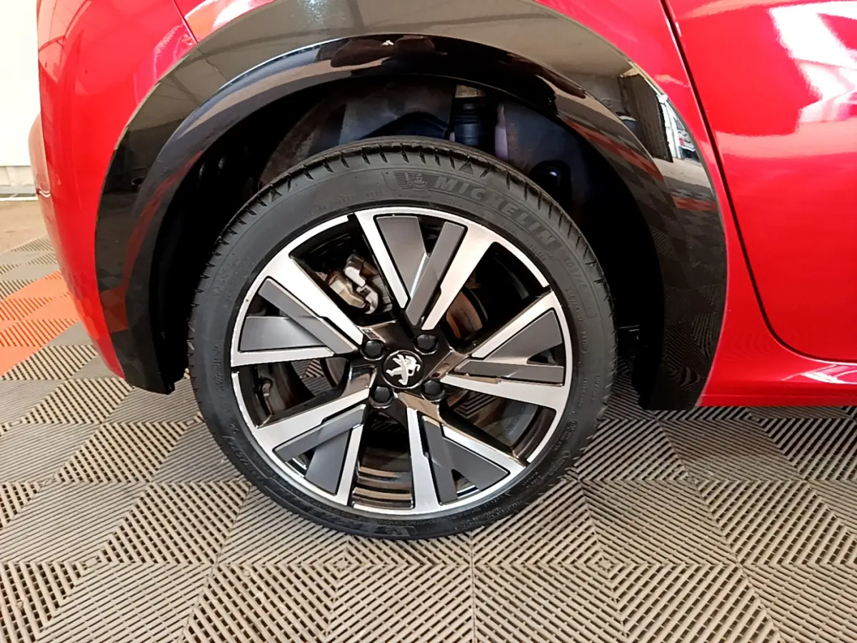 Gros plan sur la roue avant gauche de la Peugeot 208 rouge, mettant en valeur la jante alliage au design moderne.