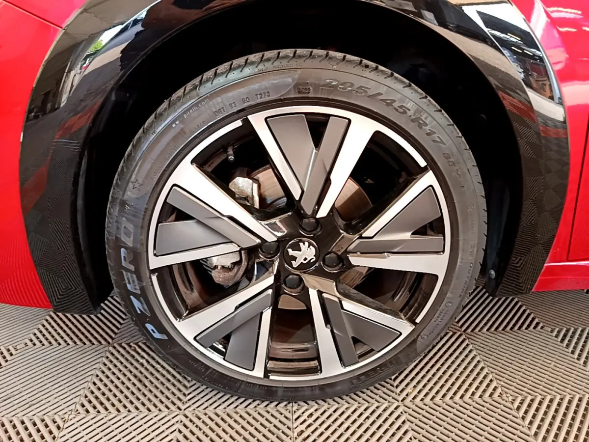 Gros plan sur la roue avant gauche de la Peugeot 208 rouge, jante alliage à design moderne et logo lion central.