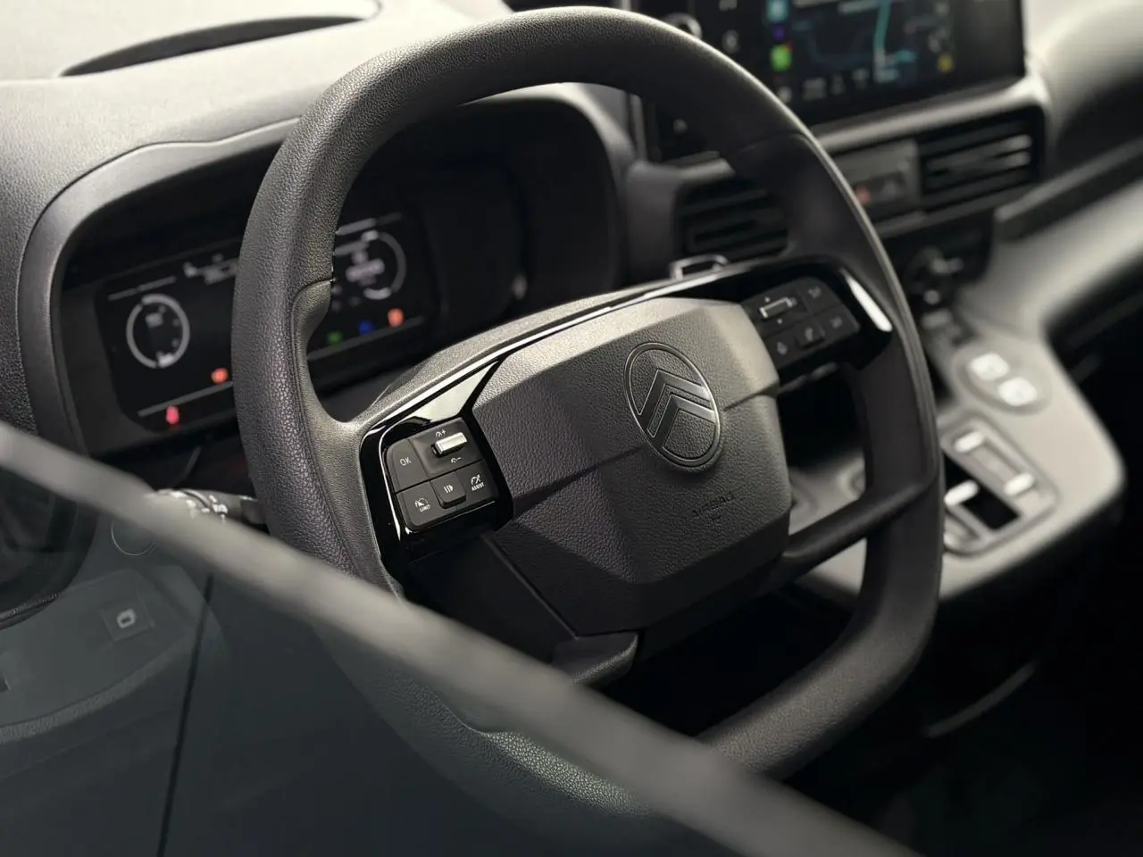 Vue rapprochée du volant multifonctions noir du Citroën Berlingo 2025 avec tableau de bord numérique en arrière-plan.