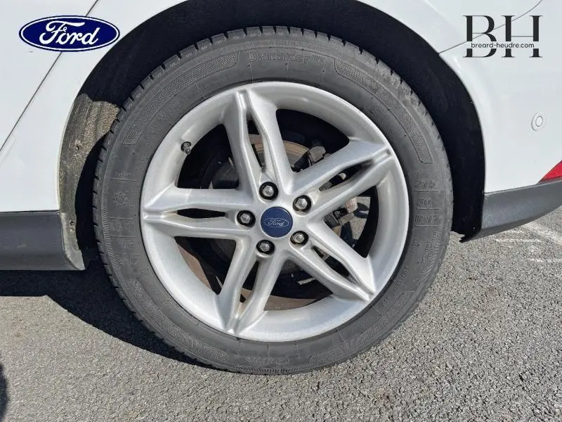 Gros plan sur la roue arrière droite d'une Ford Focus blanc glacier, avec jante alliage à cinq branches.