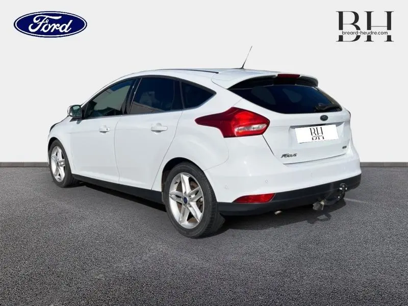 Vue 3/4 arrière droite d'une Ford Focus blanche Glacier avec becquet et jantes alu sur fond neutre.