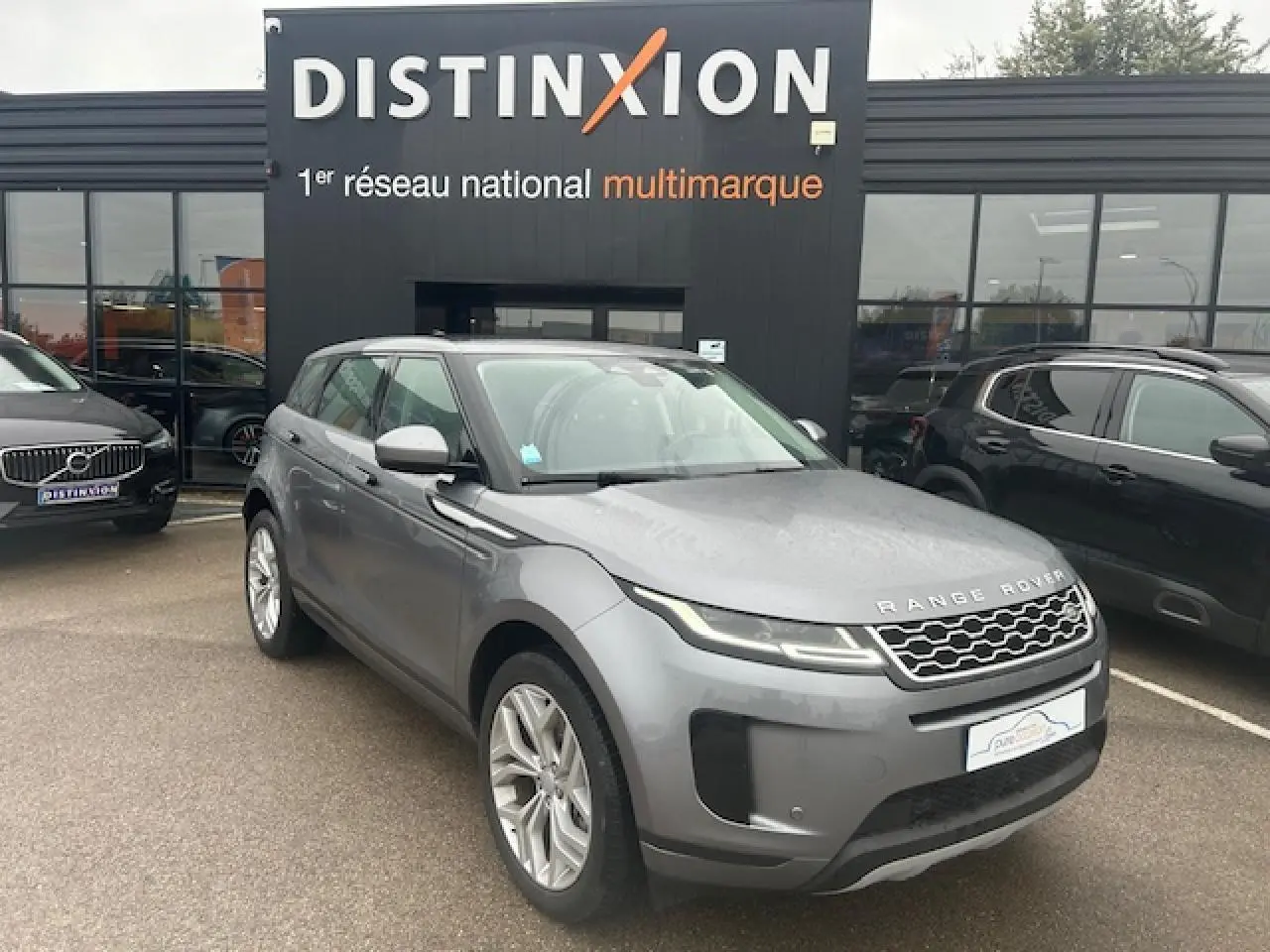 Range Rover Evoque gris foncé métallisé vu en 3/4 avant droit devant un showroom Distinxion.