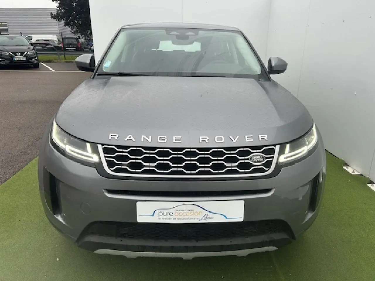 Vue de face d'un Range Rover Evoque gris foncé métallisé avec calandre hexagonale et phares LED allumés.