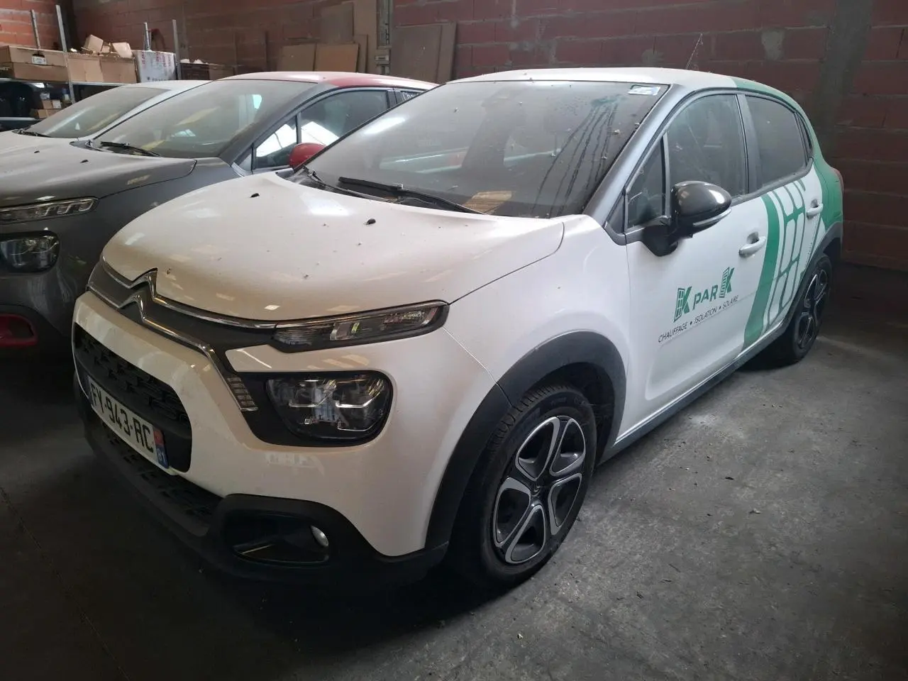 Vue 3/4 avant d'une Citroën C3 blanche avec décor vert et jantes noires dans un garage sombre