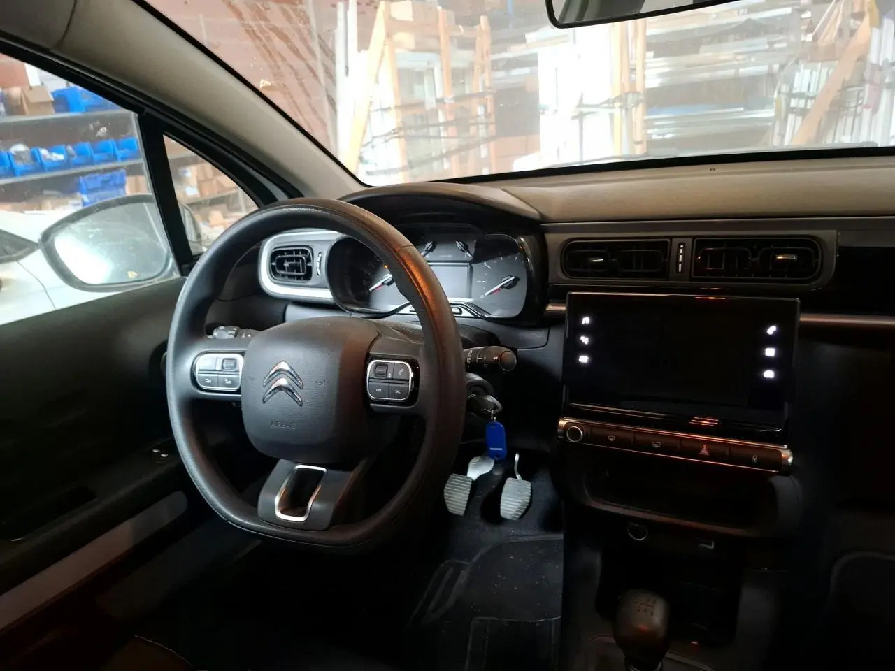 Intérieur avant de la Citroën C3 blanc banquise, volant multifonction, tableau de bord avec écran tactile et pédales visibles.