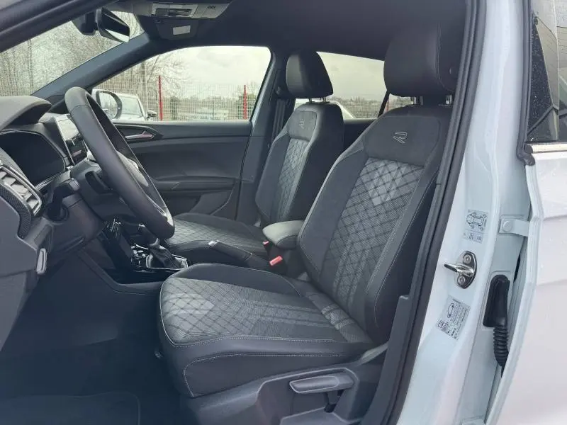 Vue intérieure côté gauche du Volkswagen T-Cross 2025 blanc Pur, sièges avant R-Line avec surpiqûres et logo R brodé.