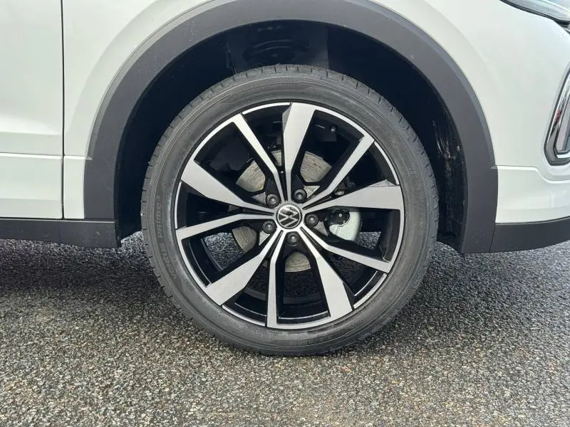 Gros plan sur la roue avant droite du Volkswagen T-Cross blanc Pur 2025, mettant en valeur la jante alliage R-Line noire et argent.