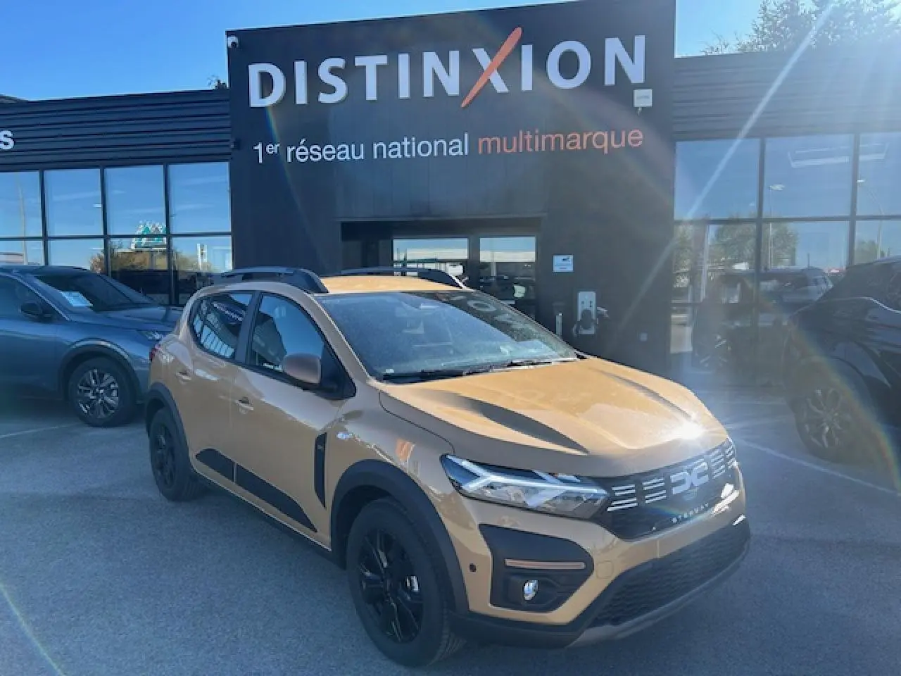 Vue 3/4 avant droite d'une Dacia Sandero Stepway beige Safari avec jantes noires et barres de toit grises.