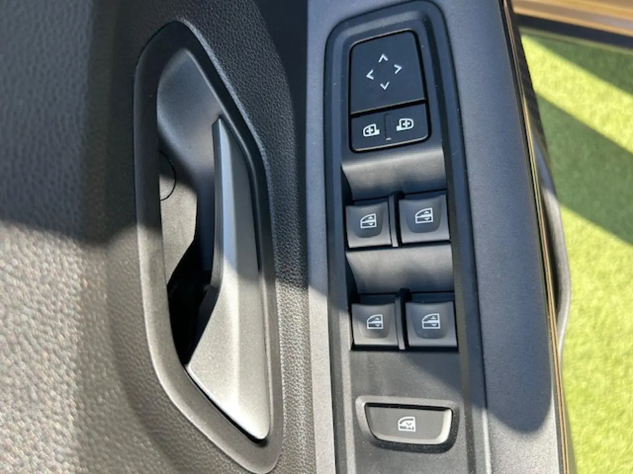 Gros plan sur la commande des lève-vitres et rétroviseurs côté conducteur de la Dacia Sandero beige Safari.