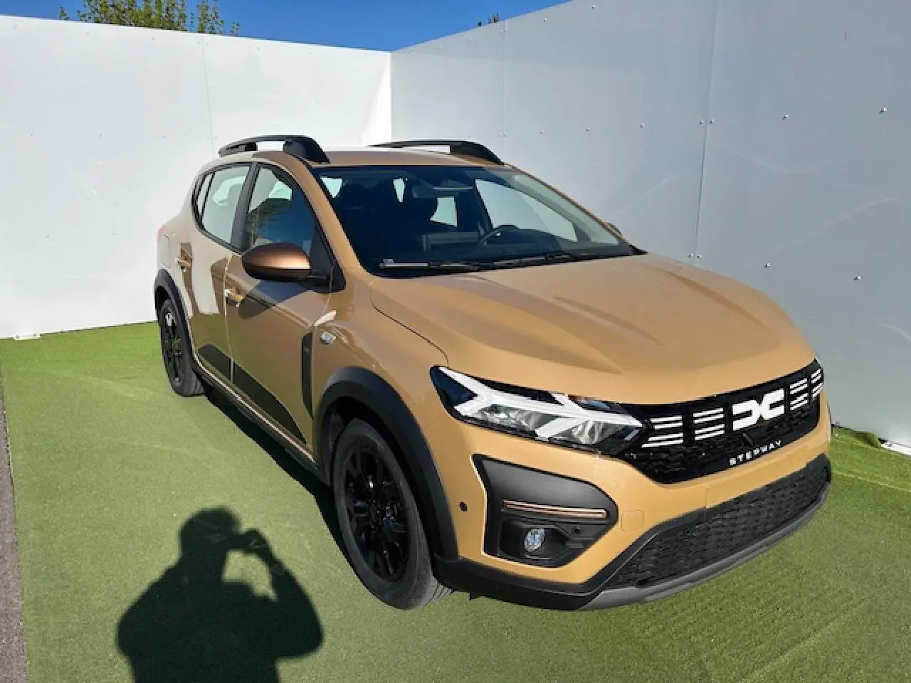 Vue 3/4 avant droite d'une Dacia Sandero III Stepway beige Safari avec calandre noire et jantes noires.