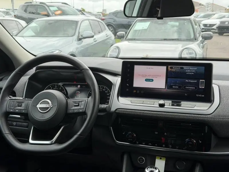 Vue intérieure du tableau de bord du Nissan Qashqai blanc nacré 2025, avec écran tactile et volant multifonction en cuir.