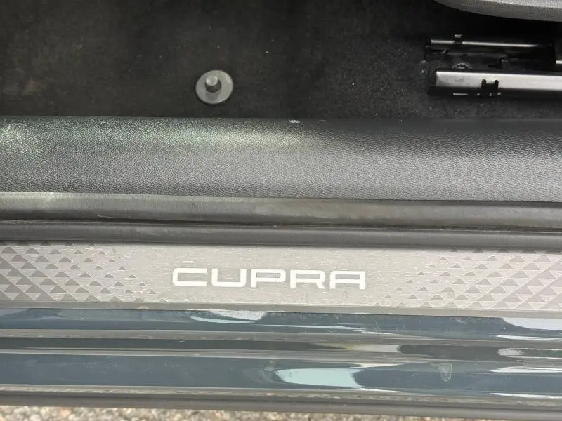 Gros plan sur la plaque de seuil de porte avec le logo CUPRA sur fond gris, intérieur noir visible.