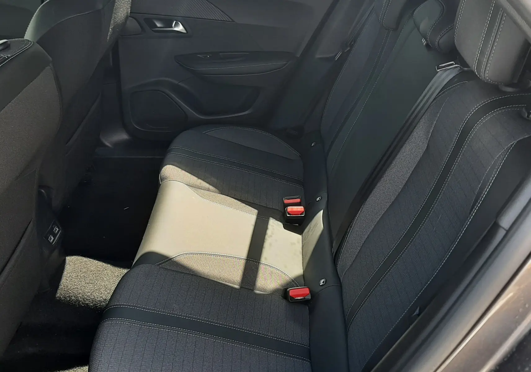 Vue latérale droite de l'intérieur arrière du Peugeot 2008 2023 avec sièges noirs et ceintures rouges visibles.