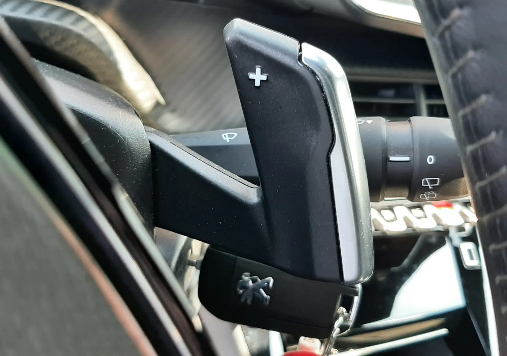 Gros plan sur la palette de changement de vitesse droite avec symbole plus dans l'habitacle noir du Peugeot 2008 gris platinium.