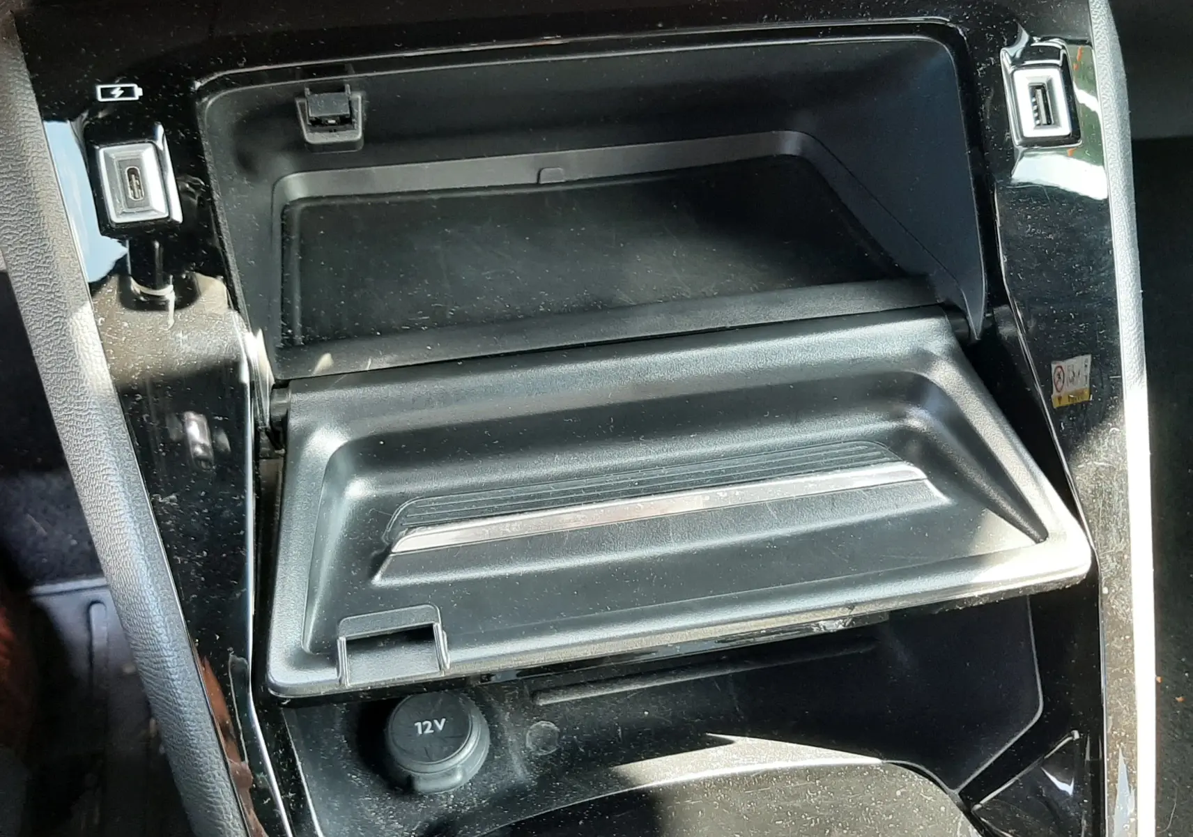 Gros plan sur la console centrale noire du Peugeot 2008 2023, montrant un compartiment ouvert et prises USB et 12V.
