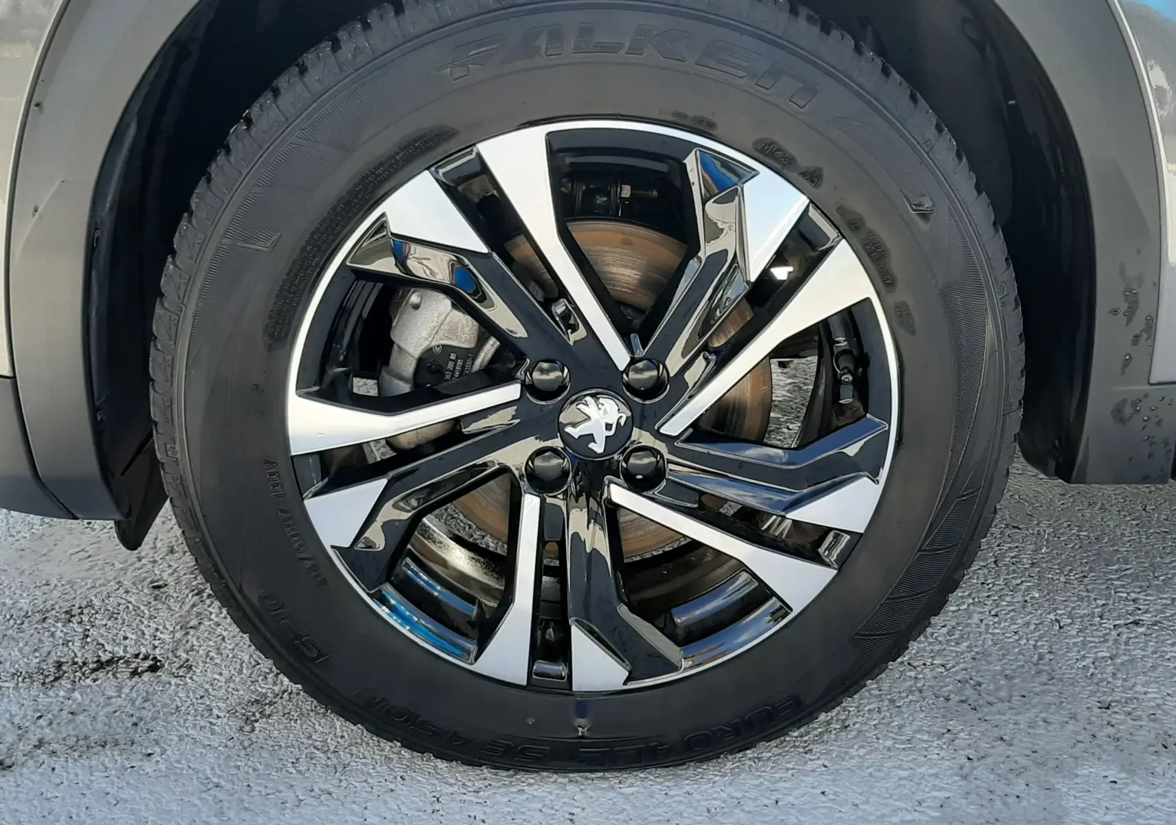 Gros plan sur la roue avant gauche du Peugeot 2008 gris platinium, mettant en valeur la jante alliage noire et argentée au design moderne.