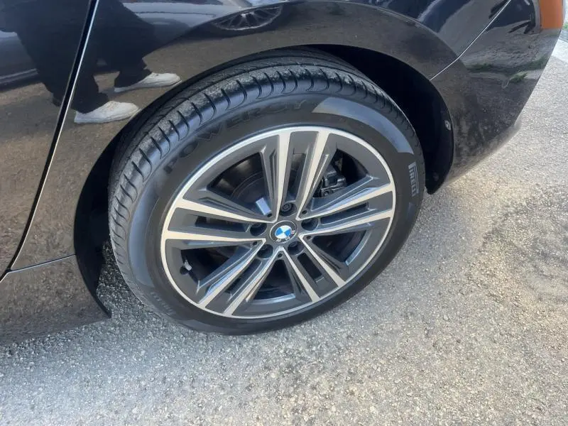 Gros plan sur la roue avant gauche noire d'une BMW Série 1 116dA avec jante alliage 5 branches et logo BMW central.