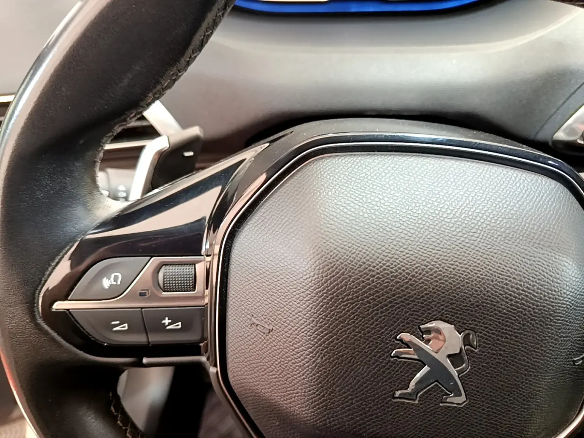 Gros plan sur le volant cuir noir du Peugeot 3008 2022 avec commandes multifonctions et logo lion central.