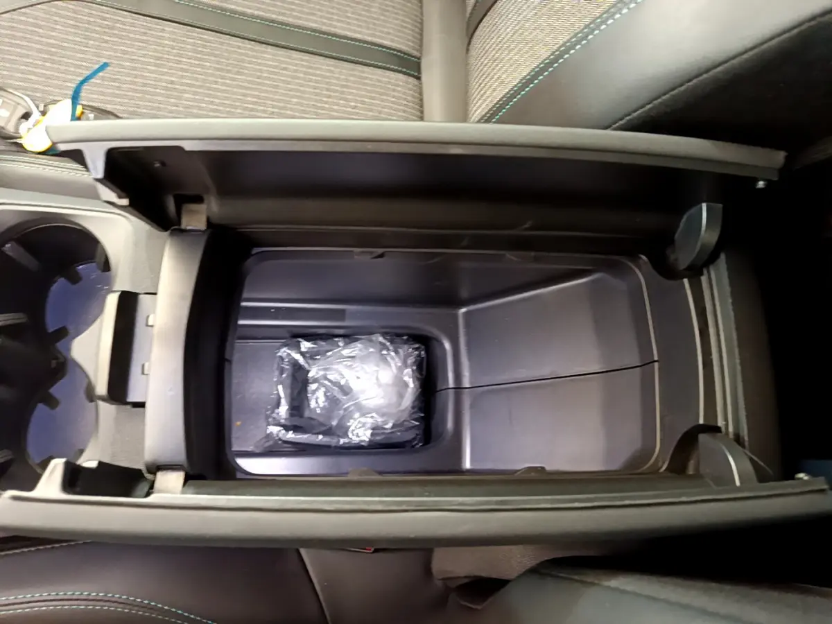 Vue plongeante sur la console centrale ouverte du Peugeot 3008 noir, montrant un rangement intérieur avec un objet emballé.