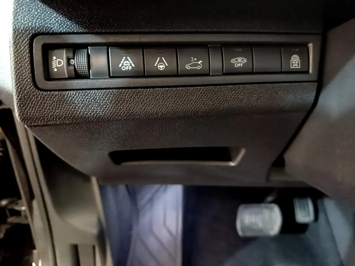 Gros plan sur les commandes d'assistance et réglage des phares du tableau de bord noir du Peugeot 3008 2022.
