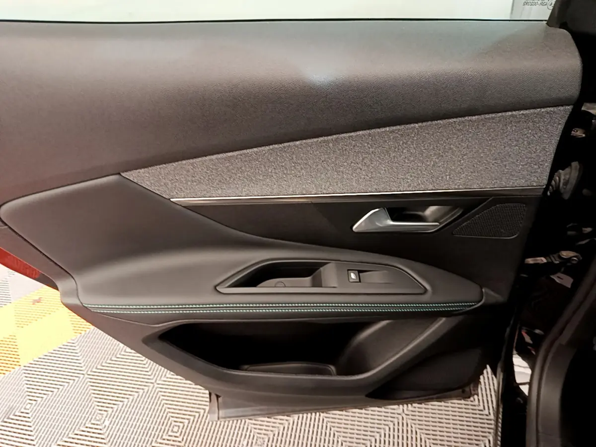 Gros plan sur la porte côté gauche intérieure du Peugeot 3008 noir, avec garniture tissu et surpiqûres bleues.