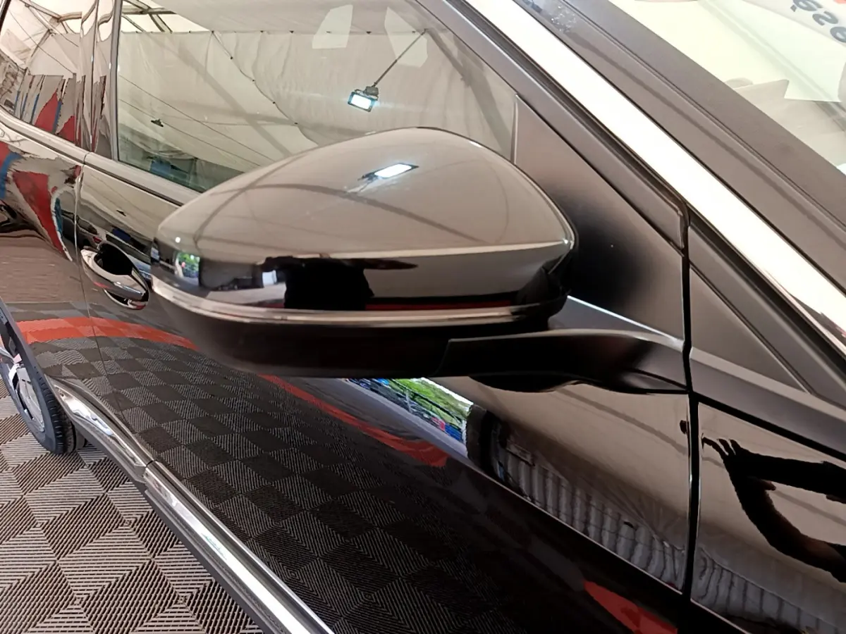 Gros plan sur le rétroviseur côté gauche d'un Peugeot 3008 noir brillant, reflétant l'environnement intérieur.