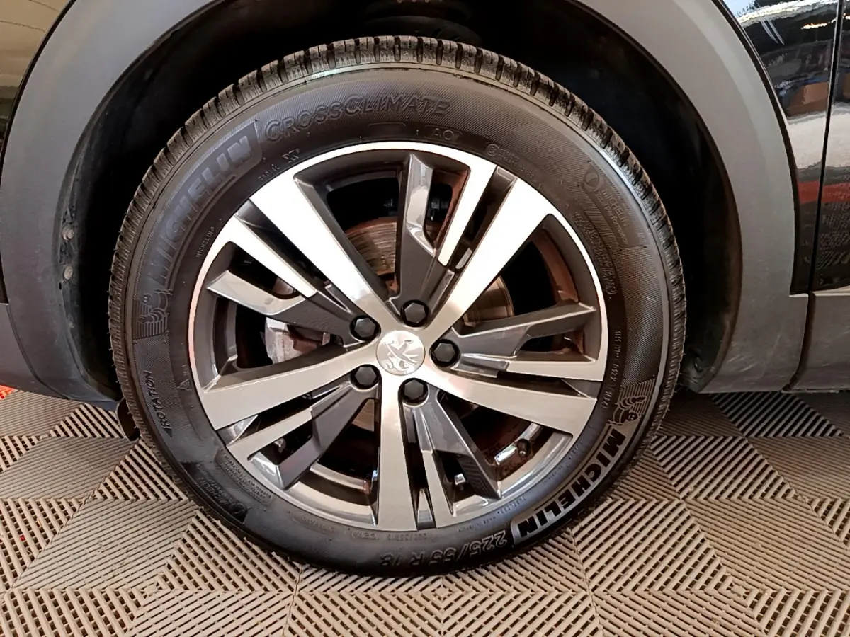 Gros plan sur la roue avant gauche du Peugeot 3008 noir, mettant en valeur la jante alliage et le pneu Michelin CrossClimate.