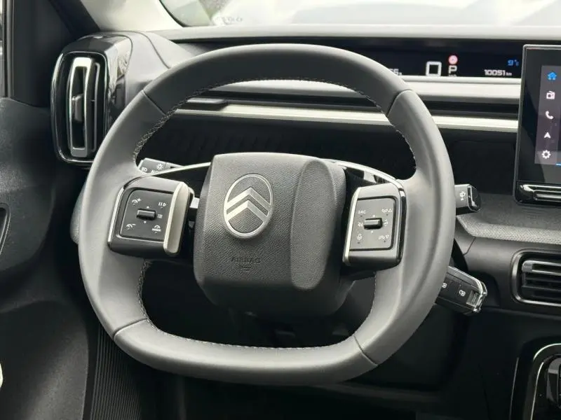 Vue rapprochée du volant gris de la Citroën C3 électrique 2025 avec commandes intégrées et tableau de bord numérique.