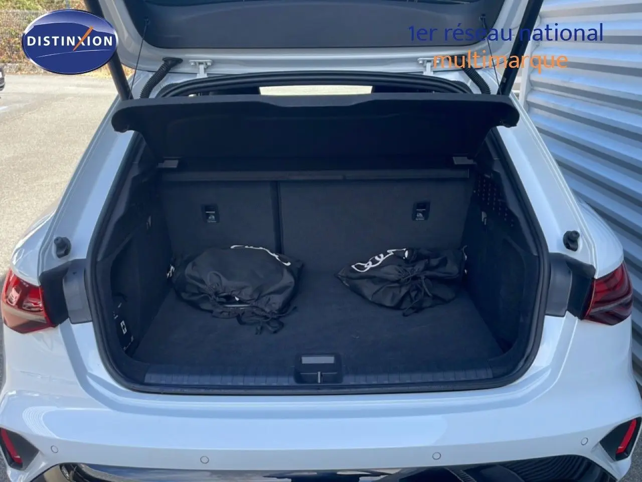 Coffre ouvert vu de l'arrière d'une Audi A3 Sportback blanc ibis 2025 avec deux sacs noirs à l'intérieur.
