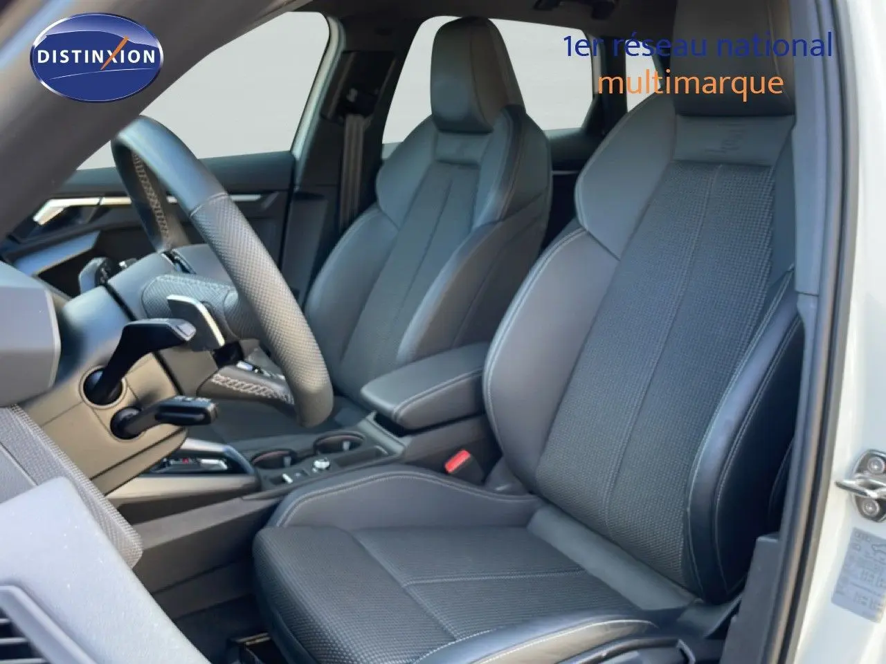 Vue intérieure côté conducteur de l'Audi A3 Sportback blanc Ibis, sièges sport gris foncé avec logo S embossé.